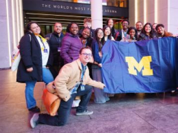 Group of UM students and Opportunity Hub staff smiling and holding a UM banner outside Madison Square Garden.